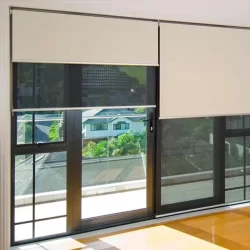 A spacious room with a wide window covered by double roller blinds