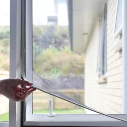A person opens a window screen to allow the sun to enter, using retractable fly screens