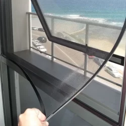 A person holding a retractable fly screen, ready to install it on a window for protection against insects