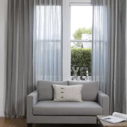 A cozy living room with a grey couch and wave fold curtains